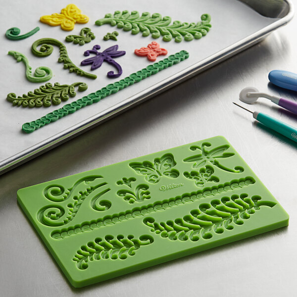 A green Wilton tray with a variety of fondant and gum paste molds and tools.