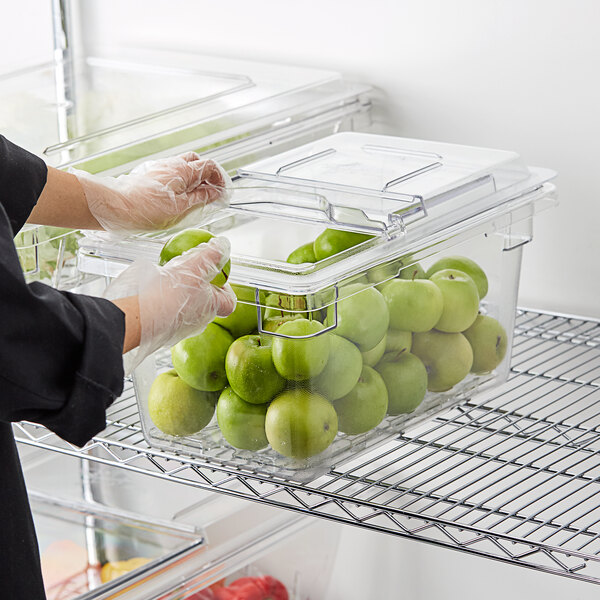A person in gloves putting green apples in a Cambro food storage container.