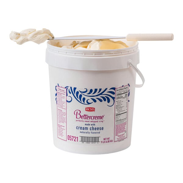 A white 9 lb. pail of Rich's Bettercreme Cream Cheese Whipped Icing with a spoon in it.