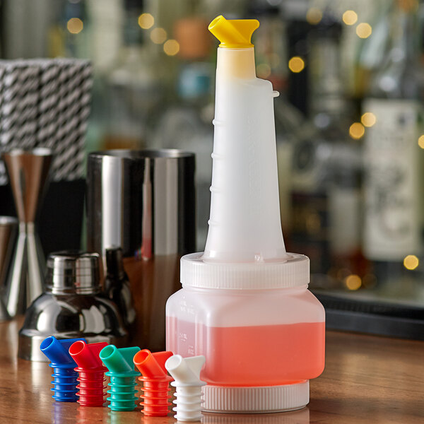 A white Vollrath plastic pour container with colored spouts on a counter next to a bottle of liquid.