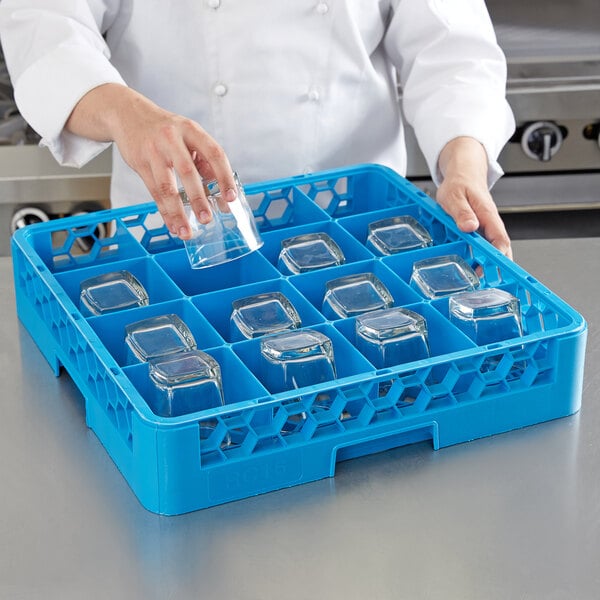 A woman in a blue chef's uniform uses a Carlisle tilted cup rack to hold clear glasses.
