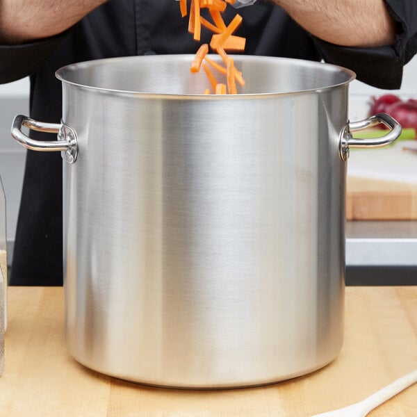 A person putting carrots into a Vollrath stainless steel stock pot.