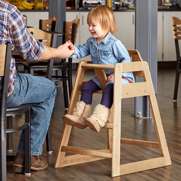 A man sitting at a table with a child in a Lancaster Table & Seating natural wood high chair.