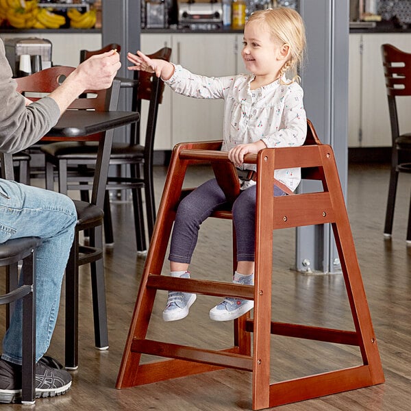 A little girl sitting in a Lancaster Table & Seating wooden high chair at a table.