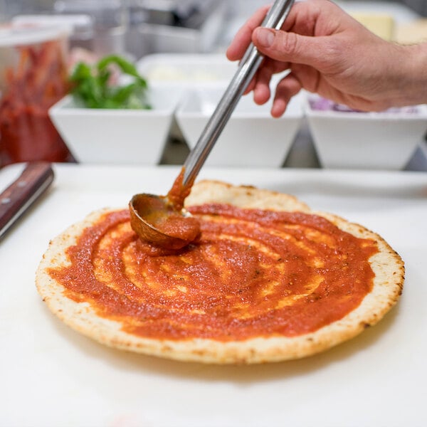 A person using a spoon to spread sauce on a Rich's gluten-free cauliflower pizza crust.
