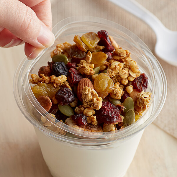 A hand holding a clear plastic Fabri-Kal parfait cup filled with yogurt, granola, and fruit.