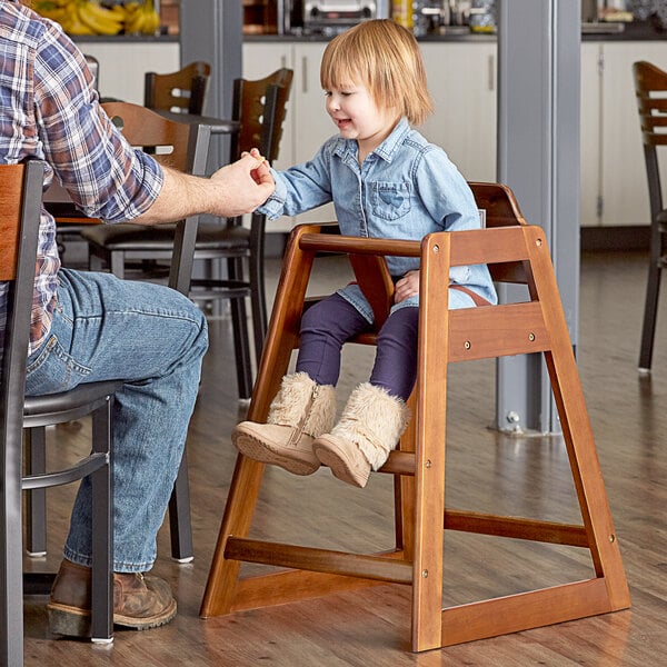 A man helping a little girl sit in a Lancaster Table & Seating wooden high chair.