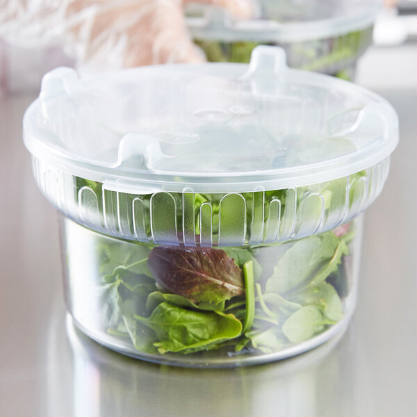 A person holding a Carlisle clear plastic crock filled with green lettuce.