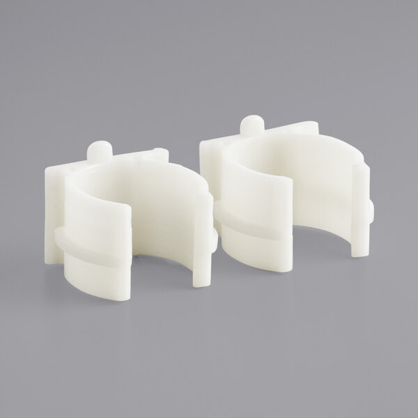 A pair of white plastic clamps on a grey surface.