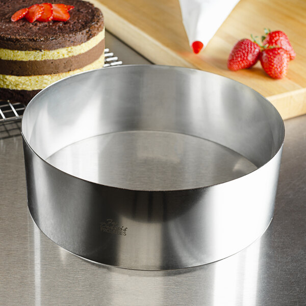 A Fat Daddio's stainless steel round cake ring on a counter with a cake in it.