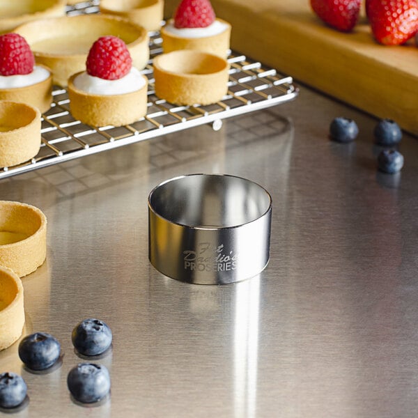 A stainless steel round cake ring filled with white cream and topped with raspberries.