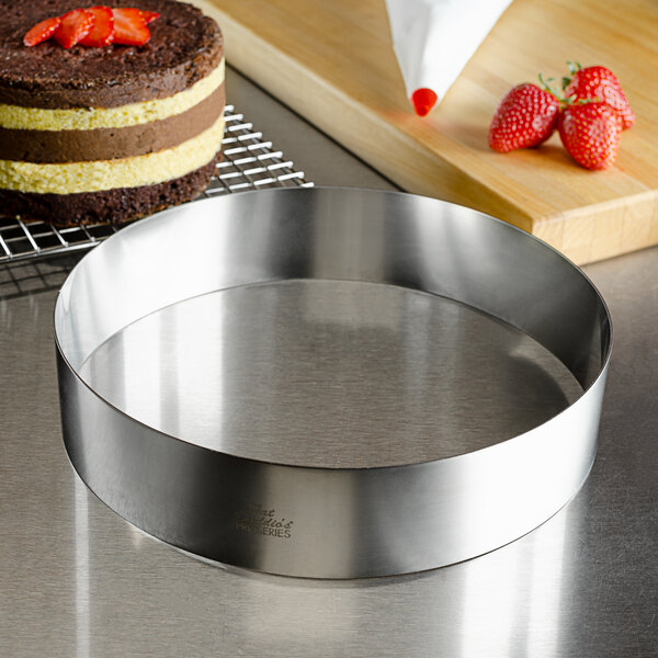 A round stainless steel cake ring with a cake topped with strawberries.