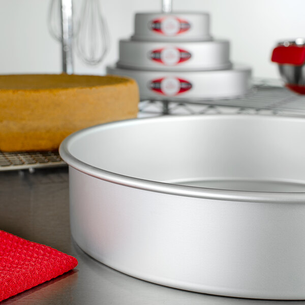 A round silver Fat Daddio's cake pan on a counter with a red towel.