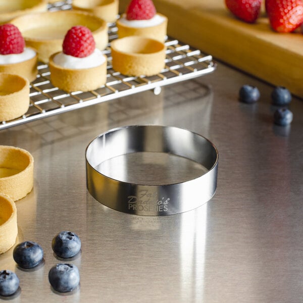 A silver stainless steel round tartlet ring on a table with small tartlets and fruit.