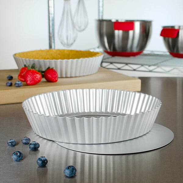 A close up of a strawberry next to a silver Fat Daddio's round fluted tart pan with a removable bottom.