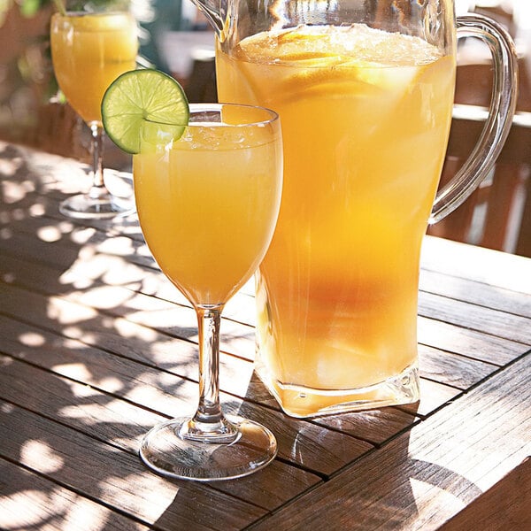 An Arcoroc Outdoor Perfect wine glass filled with orange juice on a table with a pitcher and glasses of orange juice.