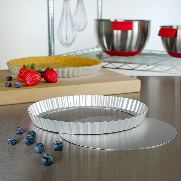 A Fat Daddio's round fluted aluminum tart pan with a removable bottom on a counter with berries.