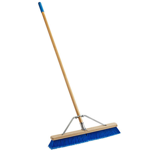A blue Carlisle commercial push broom with a wooden handle.