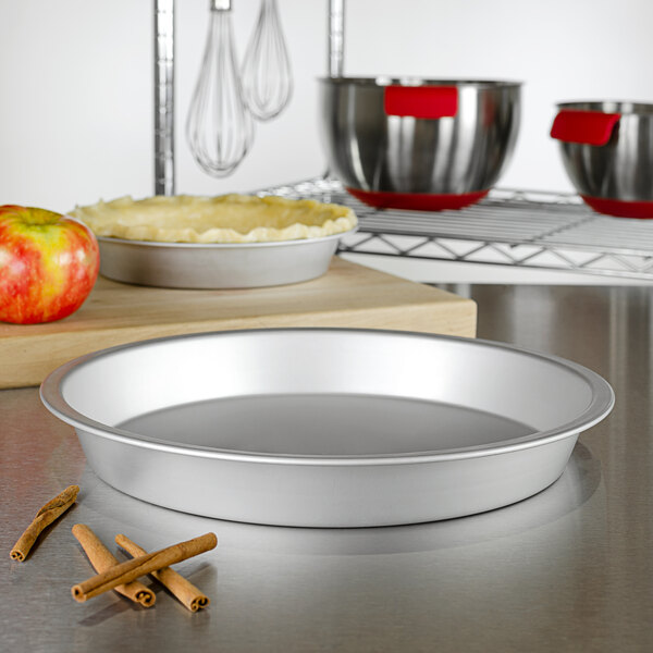A Fat Daddio's ProSeries anodized aluminum pie pan on a counter with a bowl of apples and cinnamon.