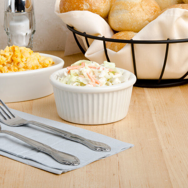 A white Tuxton fluted ramekin filled with macaroni and cheese on a table with a bowl of coleslaw.