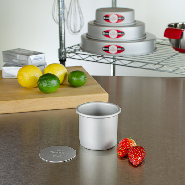 A Fat Daddio's round anodized aluminum cake pan with a removable bottom on a table with strawberries and limes.