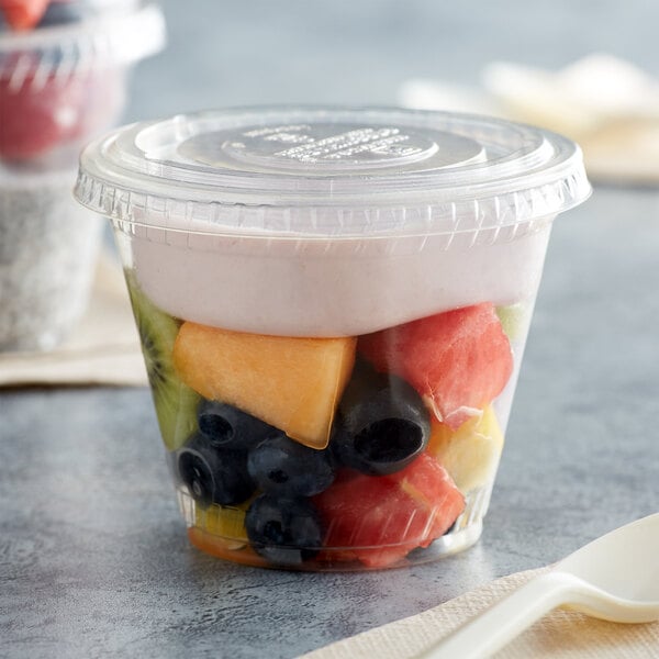 A Fabri-Kal plastic cup with fruit salad and a spoon.
