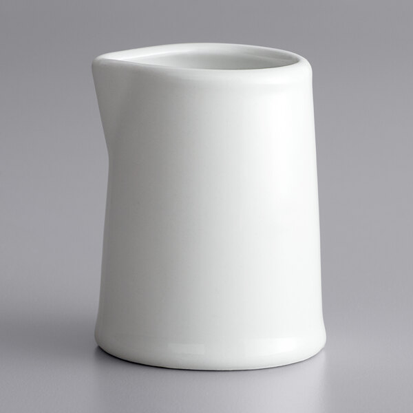 A white Corona porcelain creamer with a handle and lid on a gray surface.