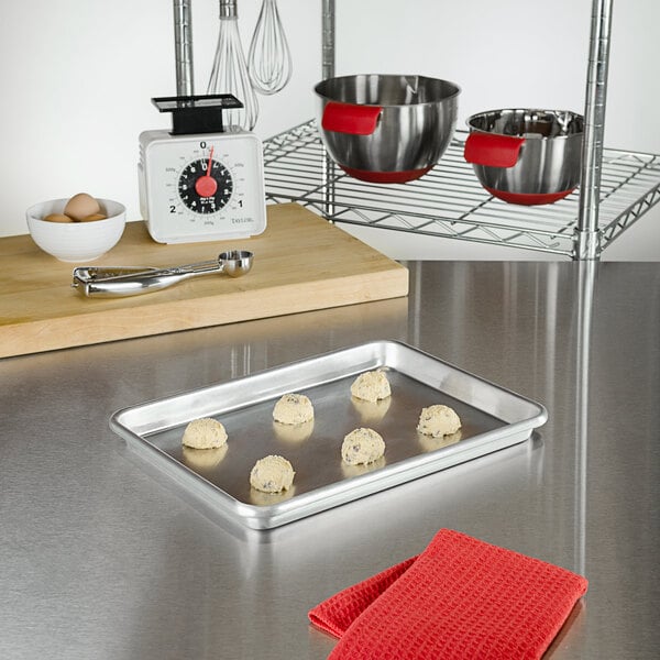 A Fat Daddio's quarter size aluminum sheet pan with cookies on it sitting on a counter.