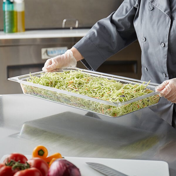 A person in a chef's uniform holding a Vigor clear polycarbonate food pan full of vegetables.