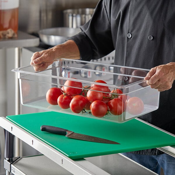 A person holding a Vigor clear polycarbonate food pan of tomatoes.