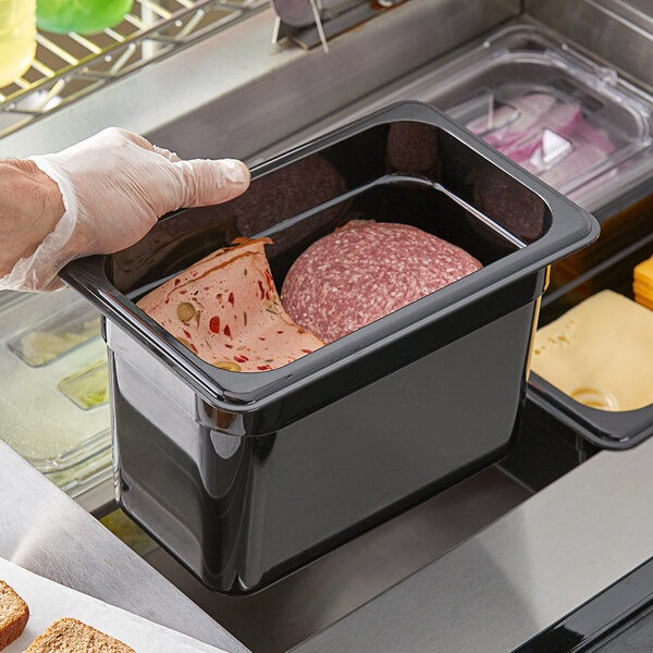 A person holding a black Vigor polycarbonate food pan filled with meat.