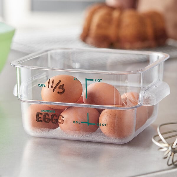 A clear Vigor square food storage container with brown eggs inside, one with writing on it.