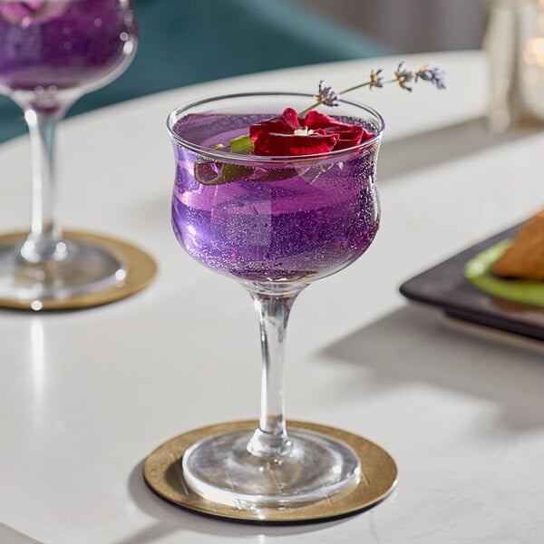 Two Acopa Deco wine glasses of purple liquid with flowers in them on a table.
