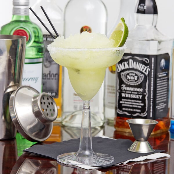 A Fineline Flairware clear plastic margarita glass with a drink and lime wedge.