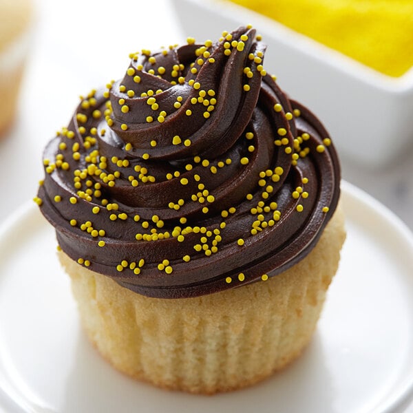 A cupcake with chocolate frosting and yellow nonpareils.