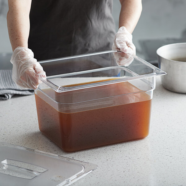 A person holding a Vigor clear plastic food pan filled with brown liquid.