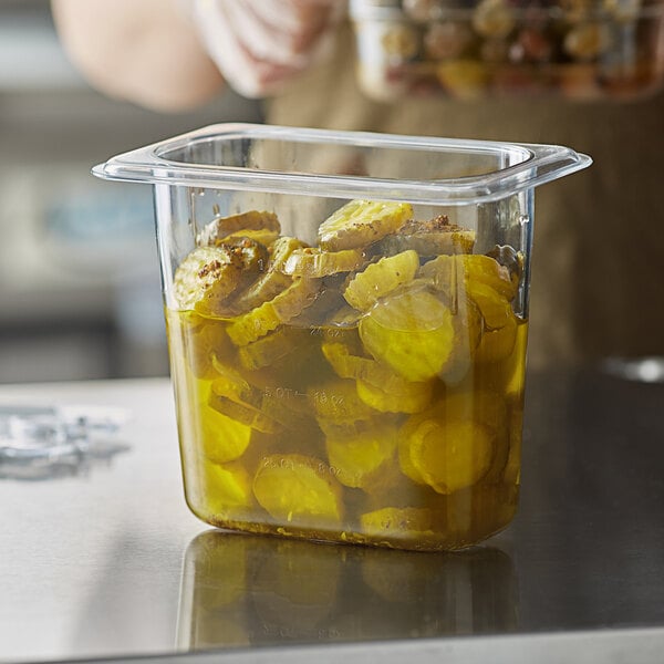 A person holding a Vigor clear polycarbonate food pan full of pickles on a counter.