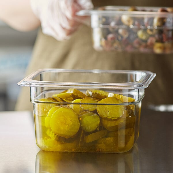 A person holding a Vigor 1/6 size clear polycarbonate food pan full of pickles.