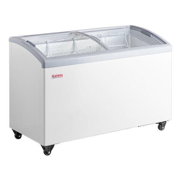 A white Galaxy curved top display freezer with glass doors on wheels.