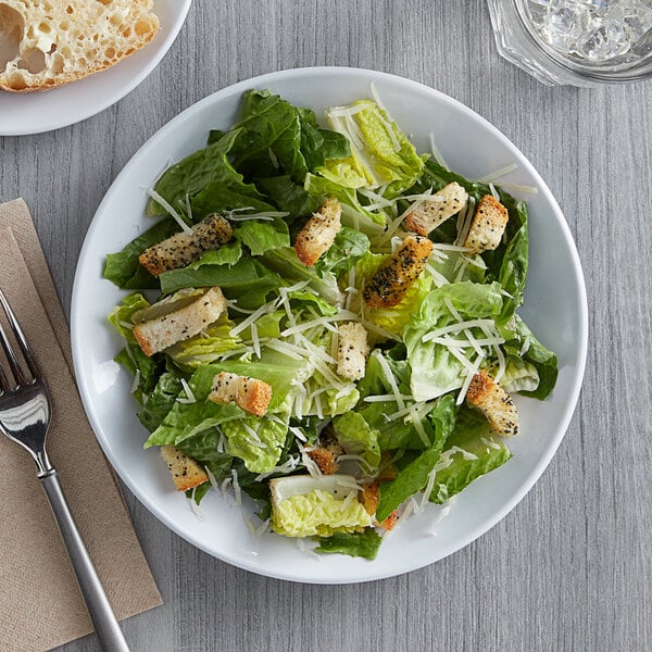 A plate of salad with croutons and parmesan cheese on a Acopa Lunar melamine plate.