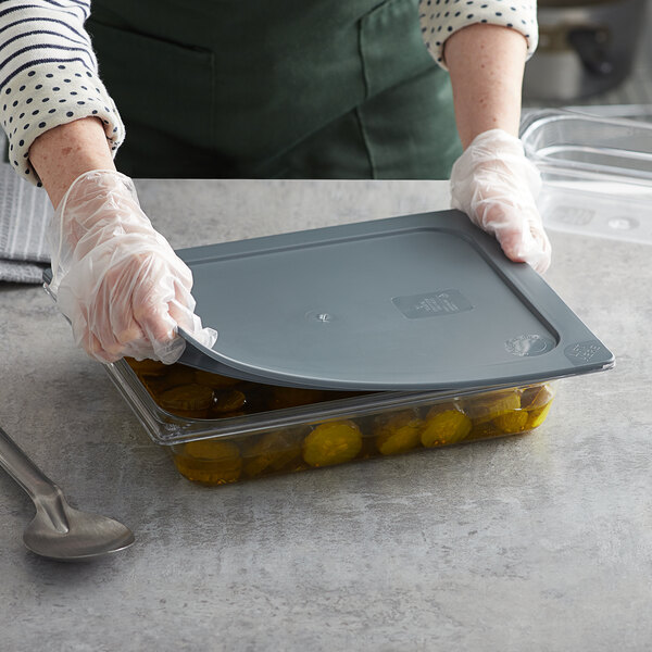 A person wearing gloves secures a Vigor gray plastic food pan with a matching lid.