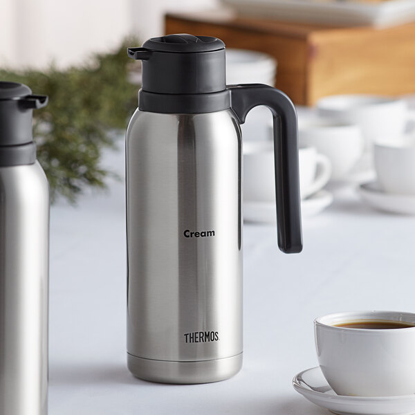 A Thermos stainless steel vacuum insulated carafe in cream with a black stripe.