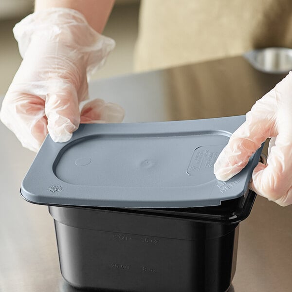 A person in gloves using a Vigor gray polyethylene lid to seal a plastic container on a counter in a professional kitchen.