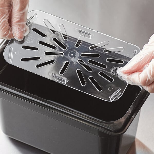 A gloved hand using a Vigor clear polycarbonate drain tray to hold a plastic container.