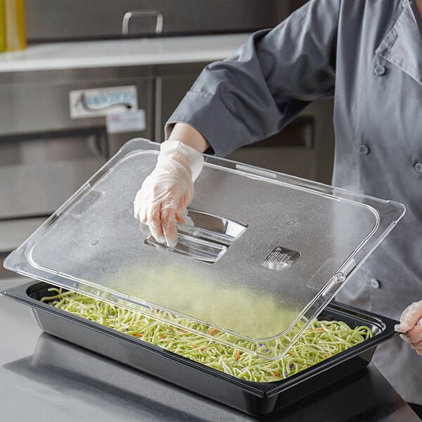 A person wearing gloves uses a Vigor clear polycarbonate food pan lid to cover food.