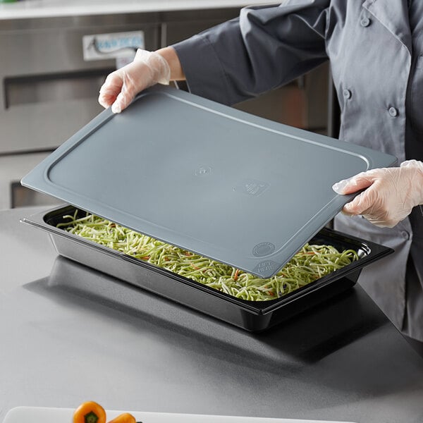 A person using a Vigor gray plastic food pan cover to seal a tray of food.