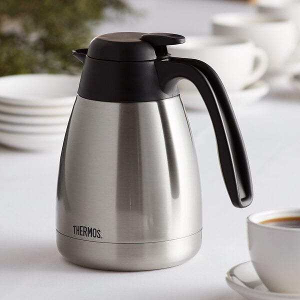 A silver and black Thermos stainless steel coffee carafe on a table.