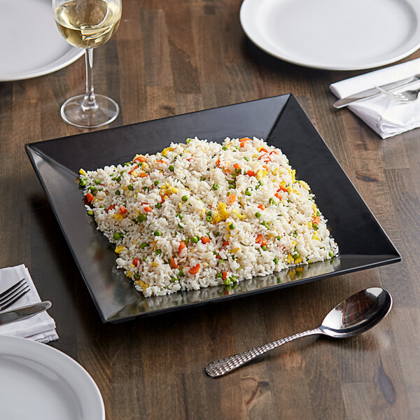 A black Acopa Rittenhouse square melamine plate with rice and vegetables on a table.