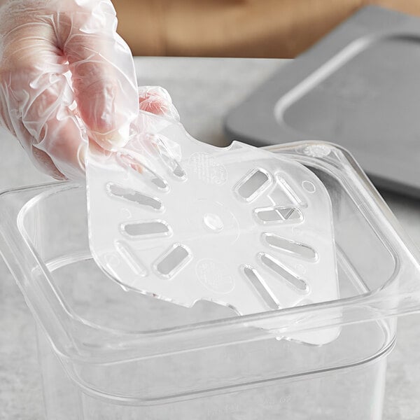 A gloved hand using a Vigor clear polycarbonate food pan drain tray on a counter.