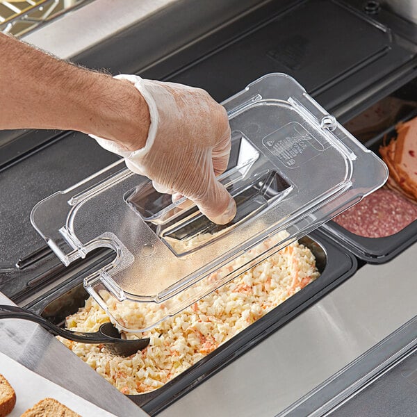 A person wearing a glove uses a clear plastic lid with a notch and handle to cover a food container.
